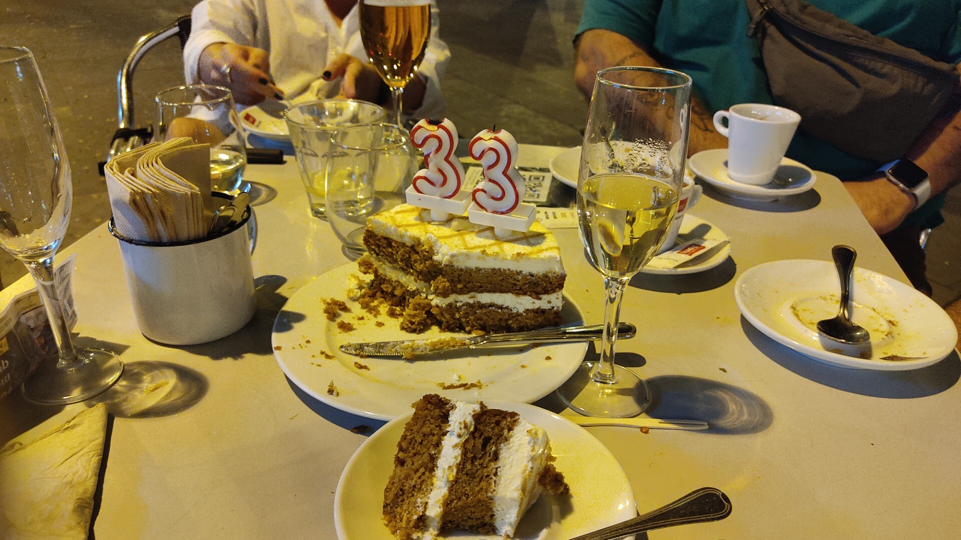 foto de una tabla en una terrassa a la nit amb un past&iacute;s de pastanaga mig menjat i una copa de cava. sobre el past&iacute;s hi ha un parell de espelmes d'aniversari que formen el n&uacute;mero trenta-tres.
