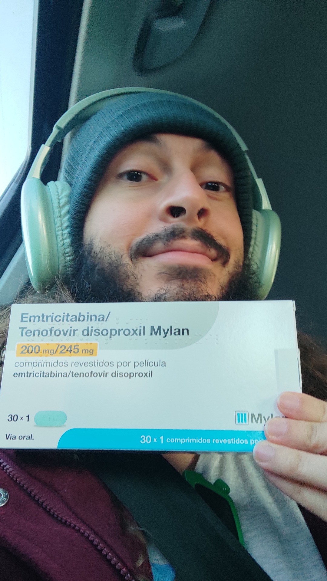 selfie em que estou vestindo um gorro verde escuro com fones de ouvido verde claro por cima. seguro uma caixa nova de 30 comprimidos de Emtricitabina/Tenofovir disoproxil da marca Mylan, tamb&eacute;m conhecida como PrEP (Profilaxia Pr&eacute;-Exposi&ccedil;&atilde;o).